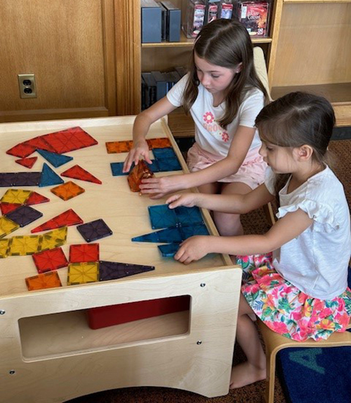 Two girls with dark hair play with colorful magnetic tiles