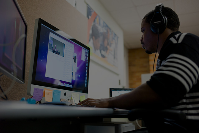 Student completing online coursework sitting in front of a computer with headphones